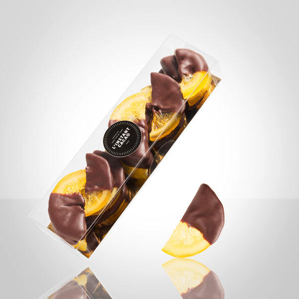 Boite de demi tranches de citrons confis enrobées en partie de chocolat noir et demi tranche de citron confit trempée en partie dans du chocolat noir