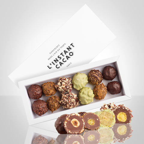 Boite de 12 rochers de Noël: noisette noir, noisette lait, pistache, physalis-pécan et céréales-feuilletine avec un rocher de chaque coupé en son milieu à côté de la boite